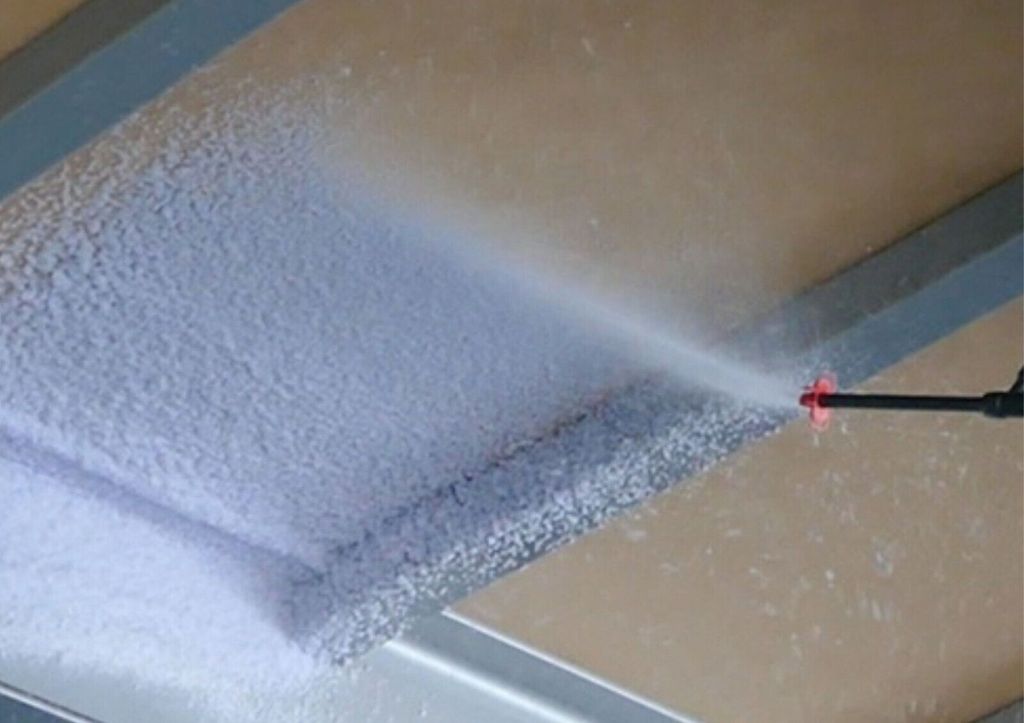A spray nozzle is spraying a white foam onto a surface, likely for insulation.
