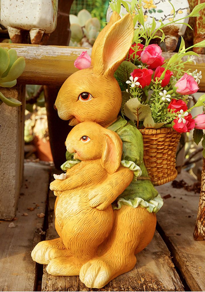 Two decorative rabbits, one larger and one smaller, are positioned on a wooden surface, with the larger rabbit holding a basket of flowers.