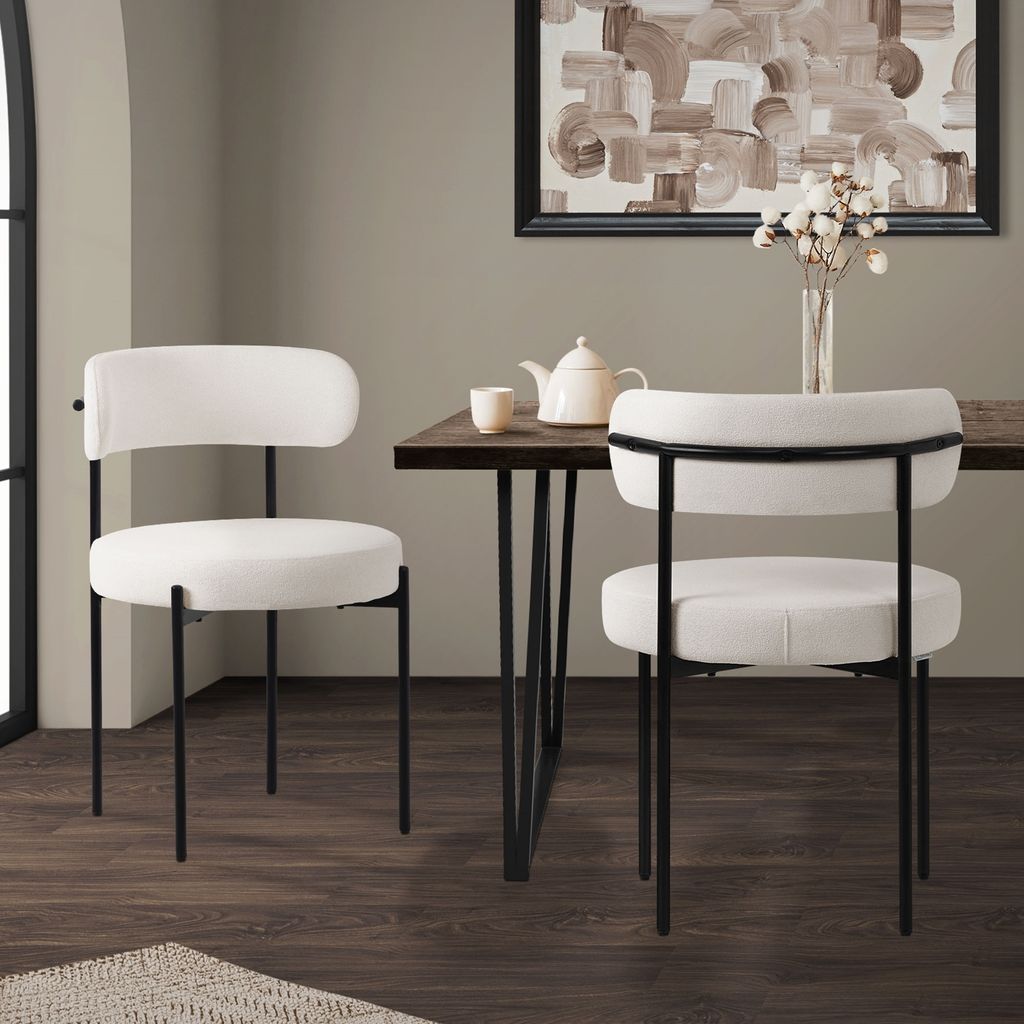 Two white dining chairs with black metal legs are placed around a wooden dining table, with a teapot and cup on the table.
