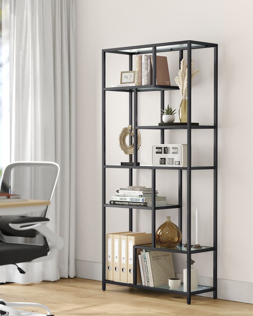 A black metal bookshelf filled with books and decorative items, placed next to a white curtain and a desk chair.