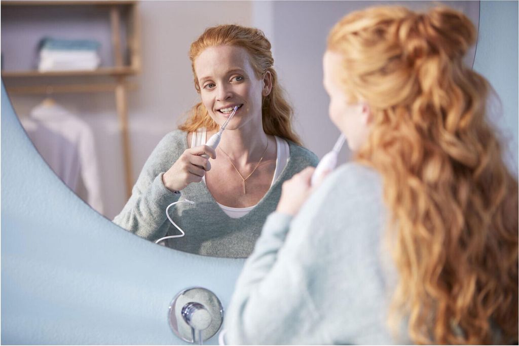 A woman is using a Philips Power Flosser in front of a mirror in a bathroom.