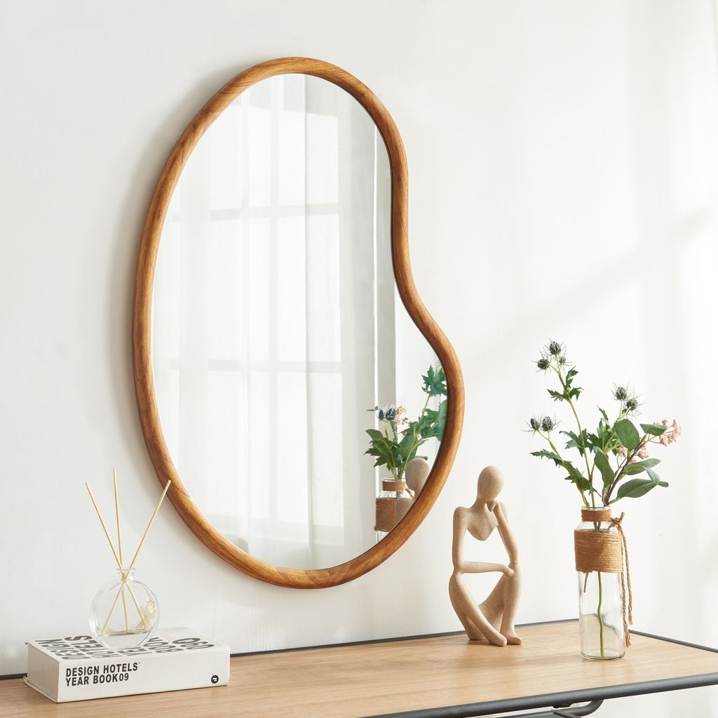 A mirror with a wooden frame is displayed on a wooden shelf, along with decorative items.