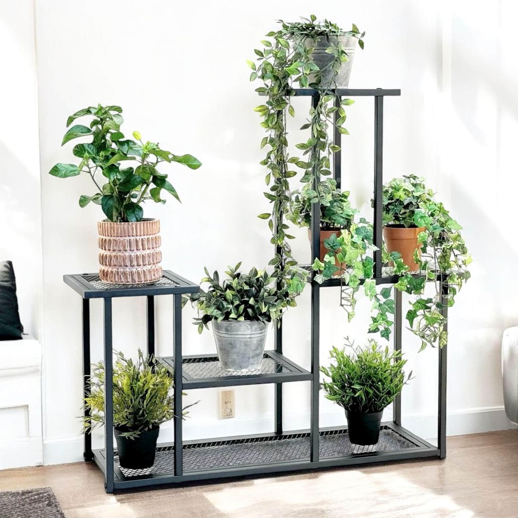 A multi-tiered metal plant stand filled with various potted plants, placed indoors against a white wall.