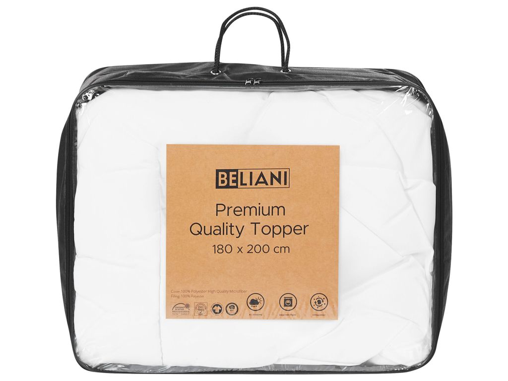 A white mattress topper is shown inside a clear plastic bag with handles. A brown cardboard tag is attached to the front of the bag.