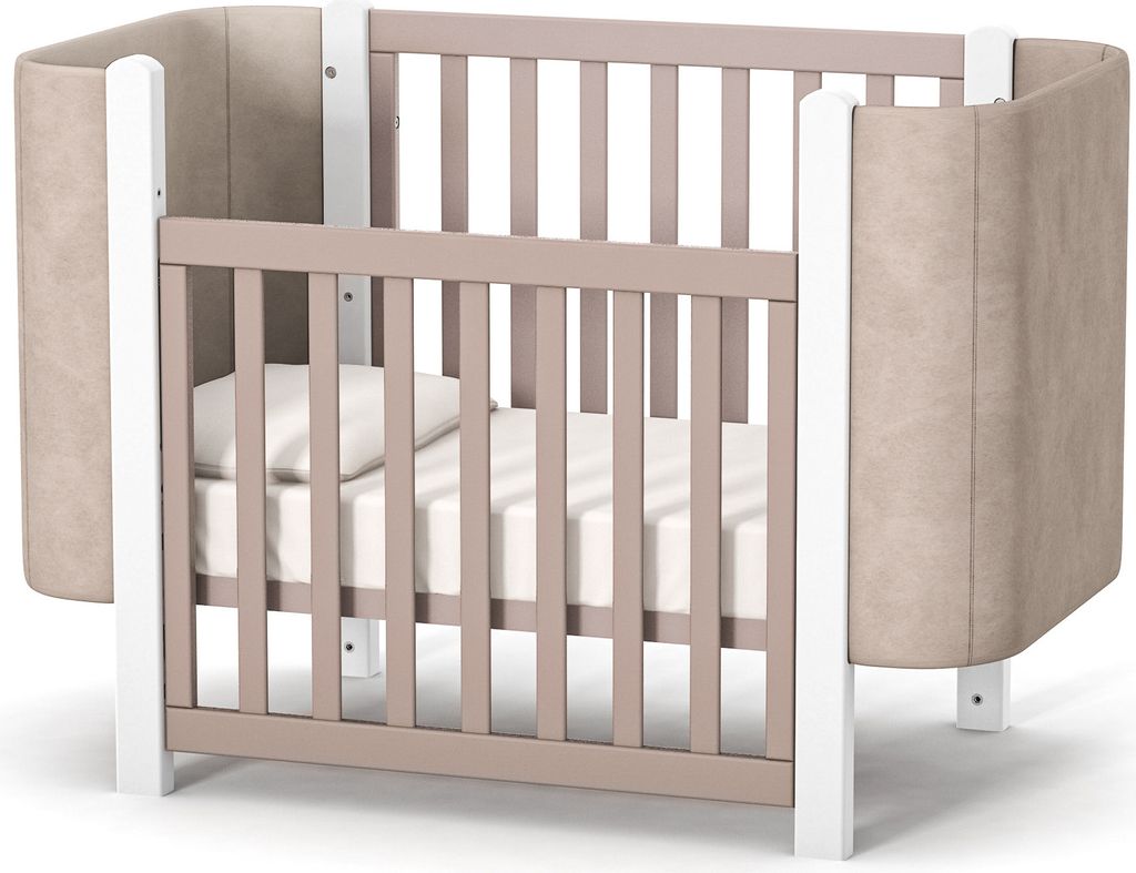 A baby crib with a mattress and pillow inside, shown from a slightly elevated side angle against a white background.