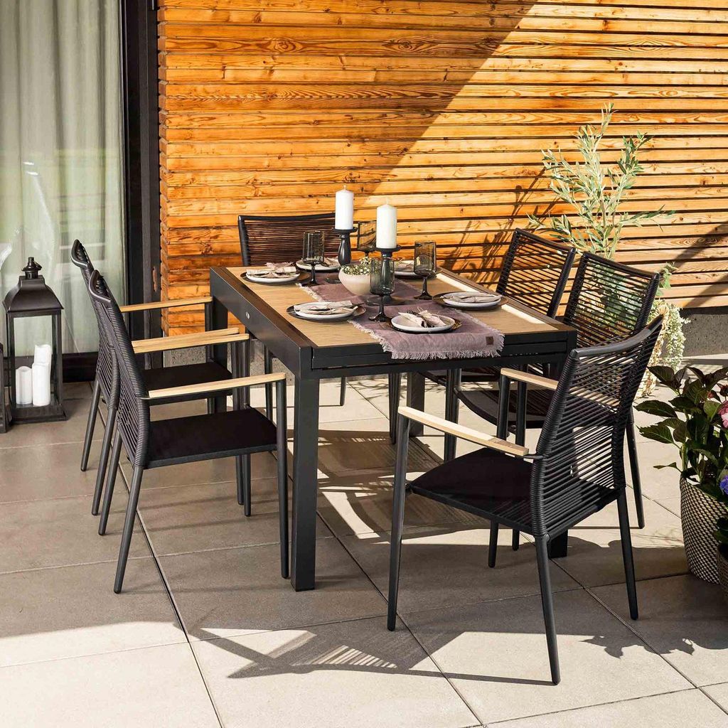 An outdoor dining set on a patio with a wooden wall background.