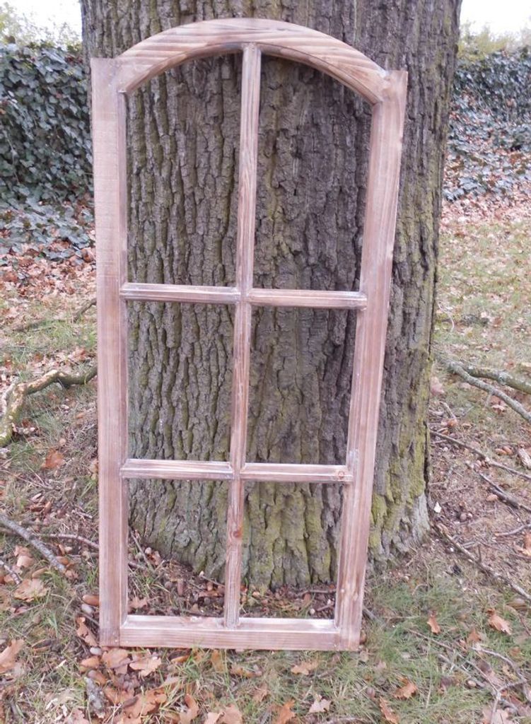 A wooden window frame leaning against a tree trunk outdoors.