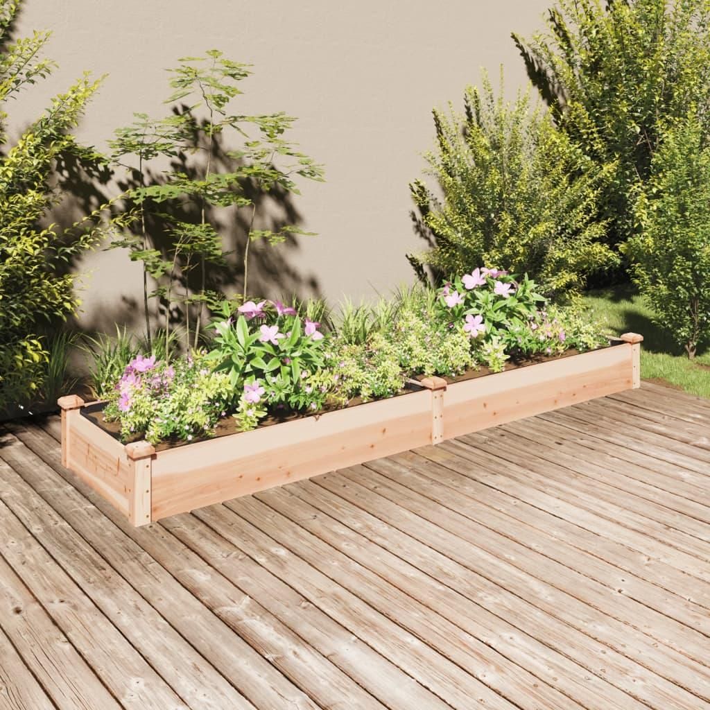 Two wooden raised garden beds filled with plants and flowers are placed on a wooden deck in front of a wall.