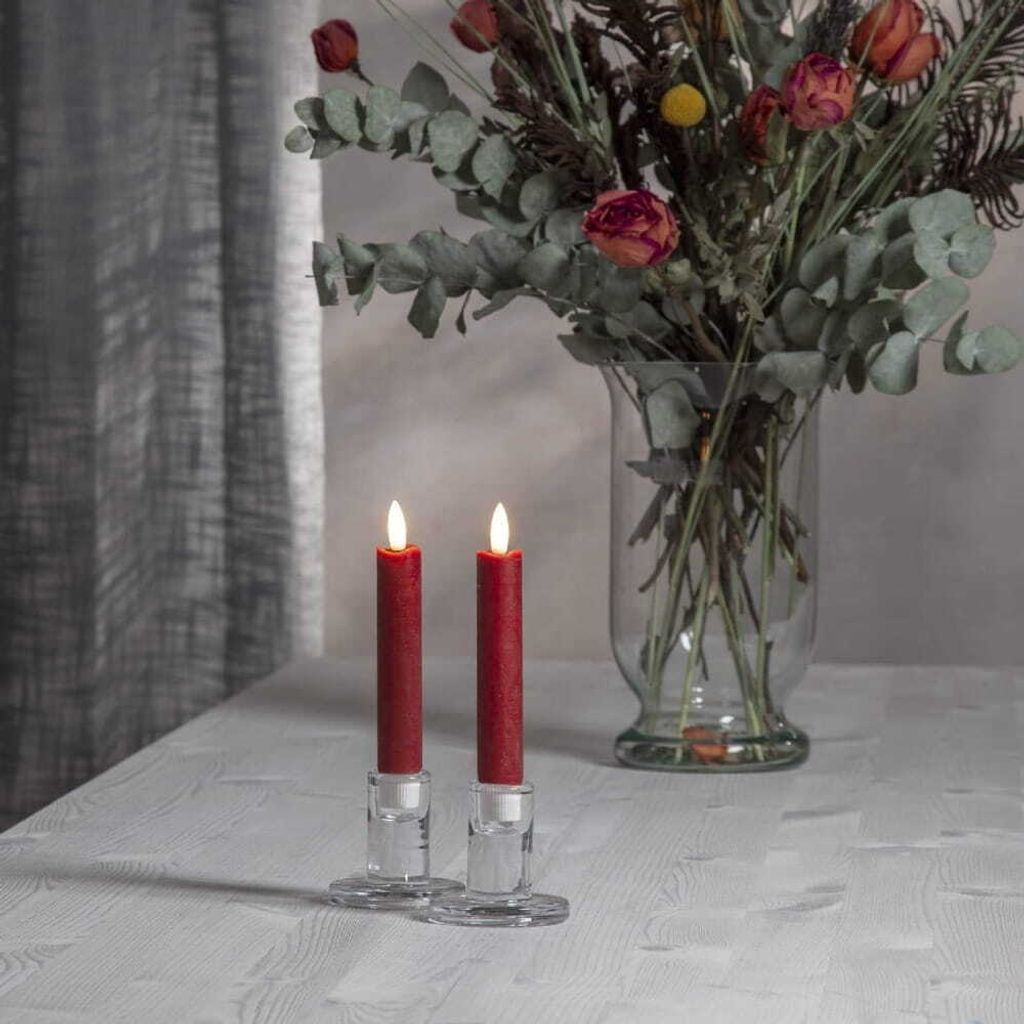Two red LED candles in glass holders on a table with a bouquet of dried flowers in the background.