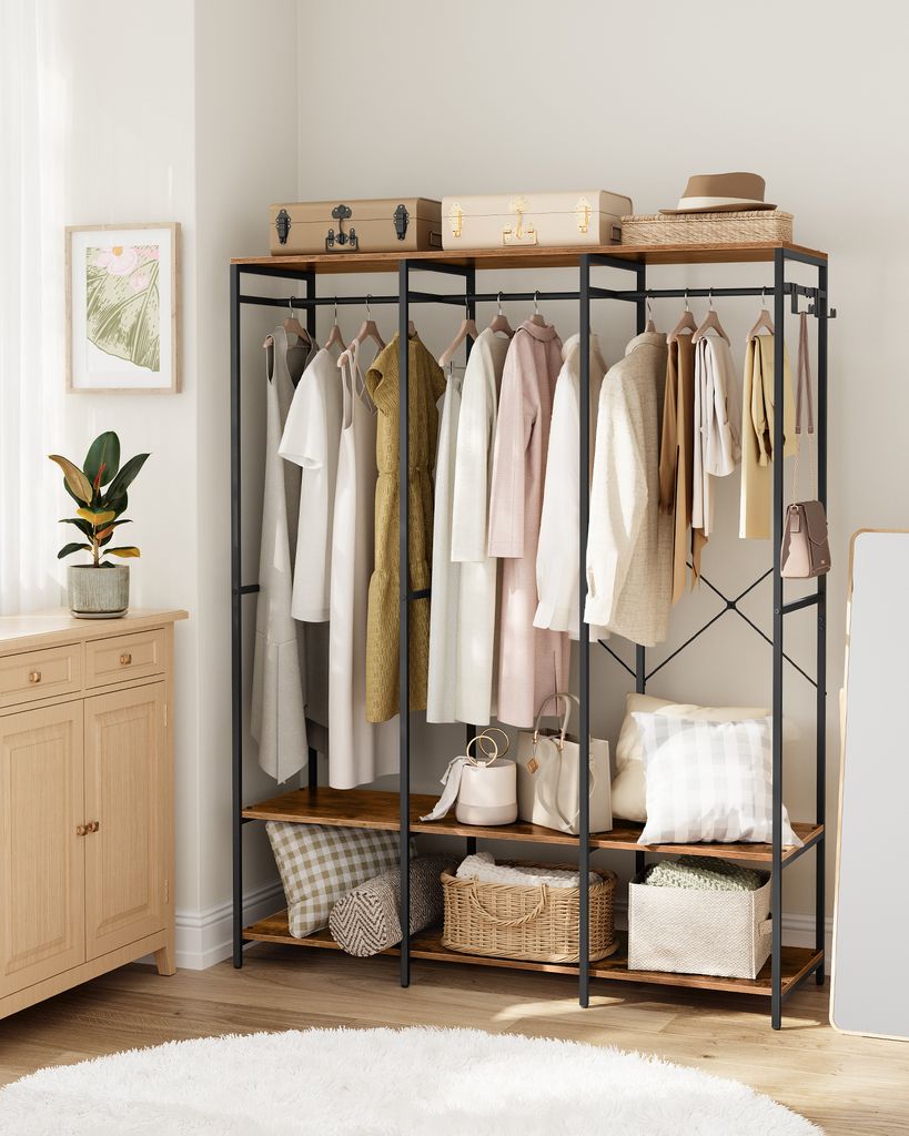 A closet rack with clothes and storage bins, placed near a wooden cabinet and a potted plant.