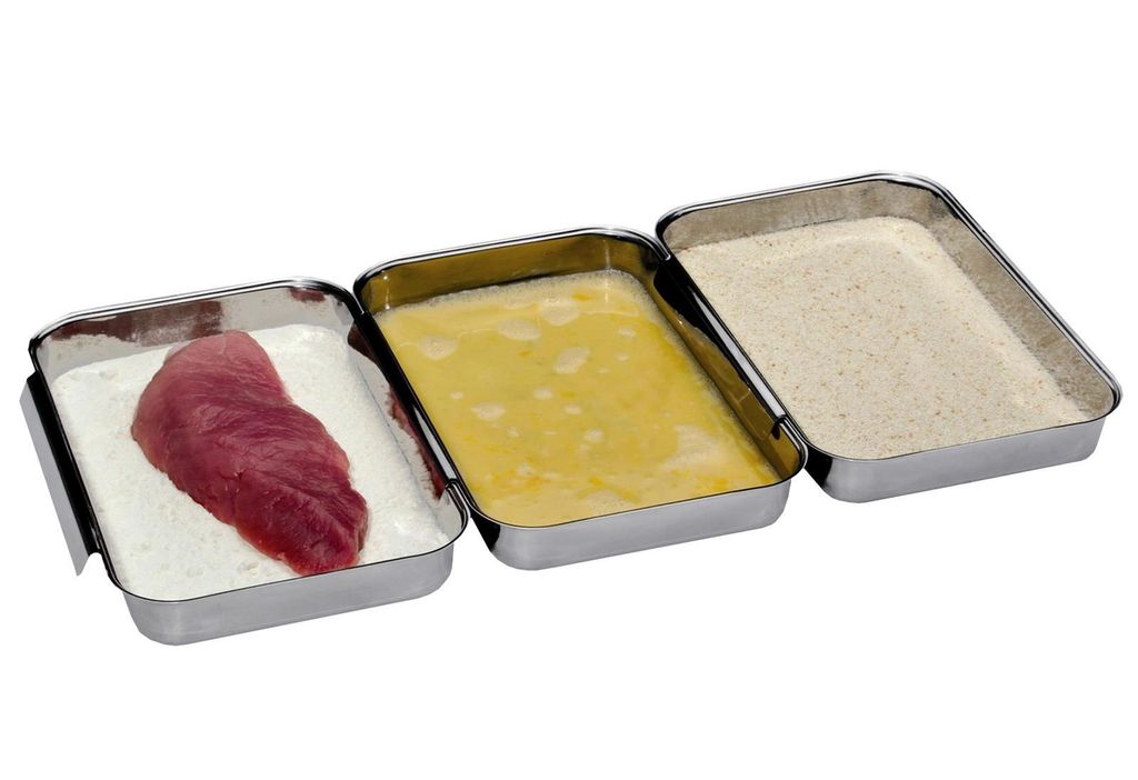 Three stainless steel trays are arranged side-by-side, with a piece of raw meat in the first tray, a beaten egg mixture in the second, and breadcrumbs in the third.
