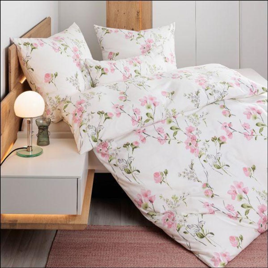 A close-up view of a bed with floral patterned bedding, a bedside table with a lamp, and a rug.