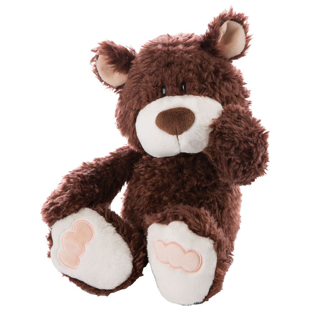A brown teddy bear is sitting with its legs extended and one paw raised to its face.