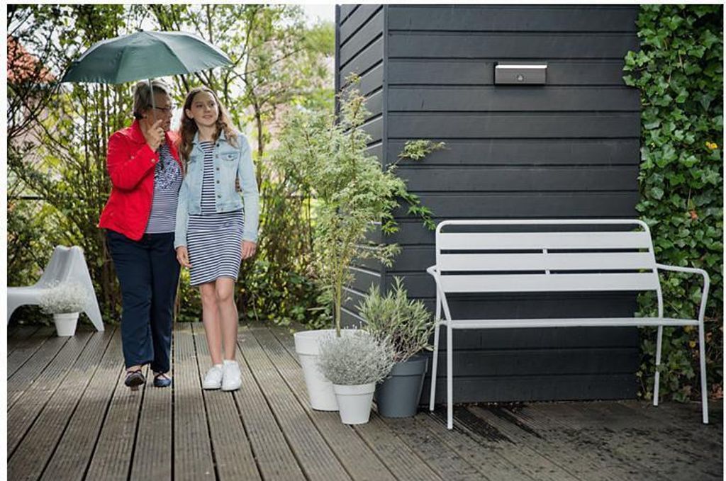 Two people walking under an umbrella on a wooden deck next to a modern house.