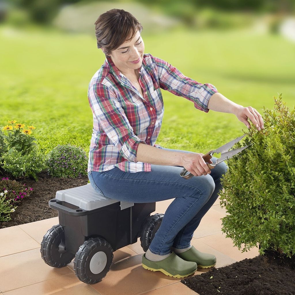 A woman is gardening while sitting on a wheeled garden cart.