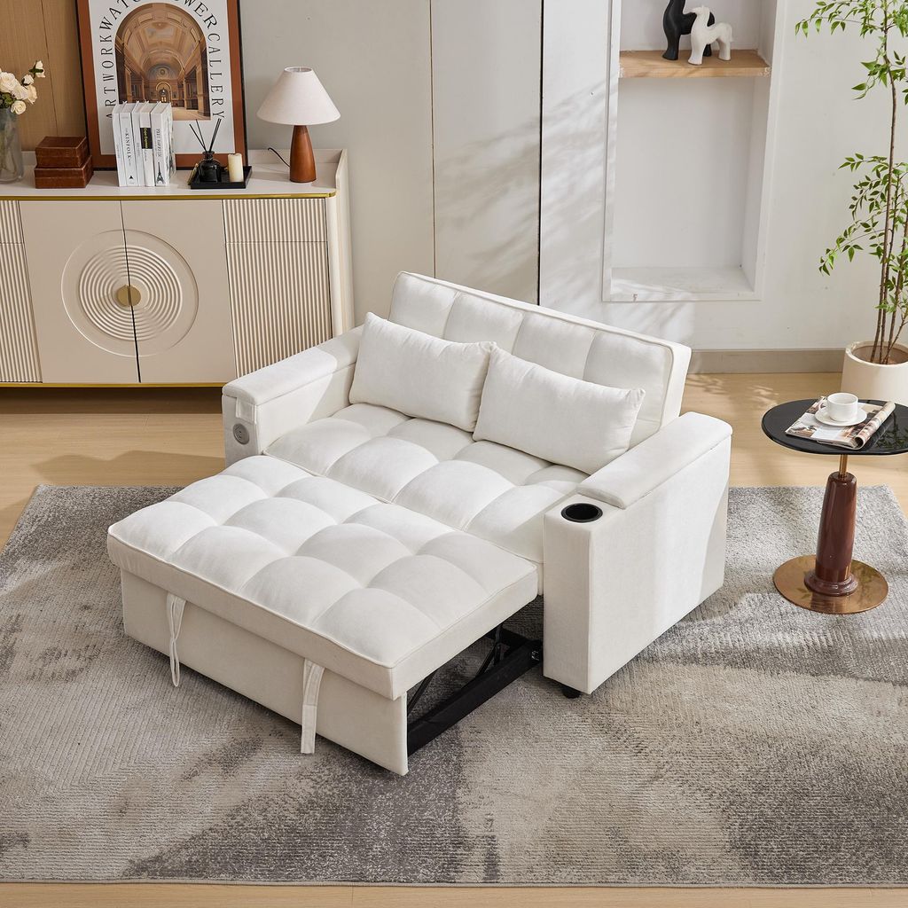 A white sofa bed is shown in a living room setting, with a side table and a cabinet in the background.