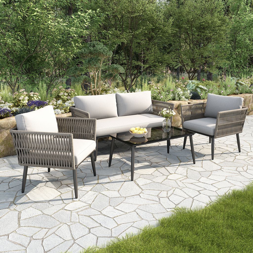 A four-piece outdoor furniture set on a stone patio surrounded by greenery.