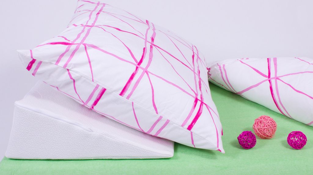 A wedge pillow with a pink patterned pillowcase rests on a light green surface, with three decorative balls nearby.