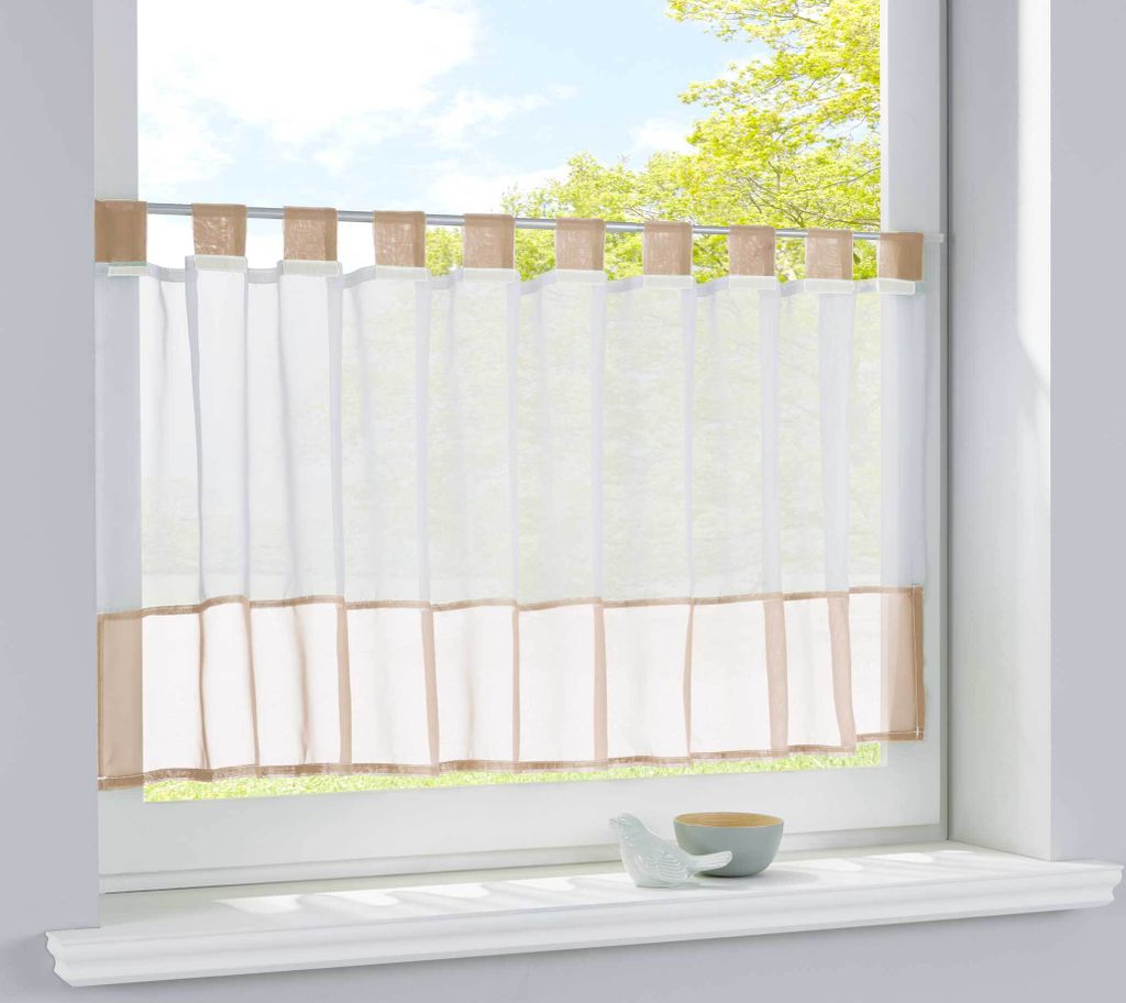 A sheer curtain with a border hangs in a window.