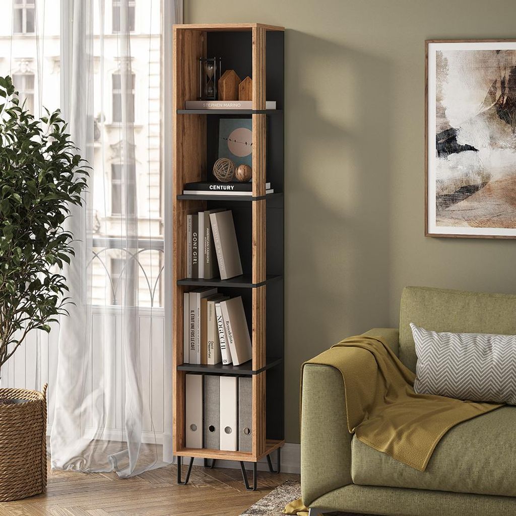 A tall, narrow bookshelf filled with books and decorative items, placed next to a window with sheer curtains and a green sofa with a yellow throw blanket.