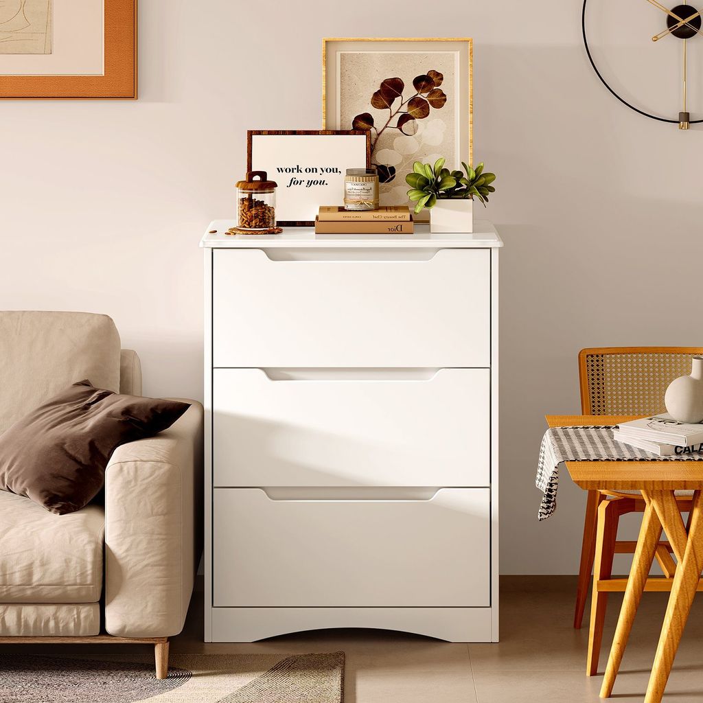 A white dresser with decorative items on top, next to a sofa and a chair with a table.