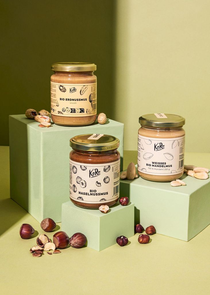 Three jars of nut butter are displayed on green cubes, surrounded by nuts.