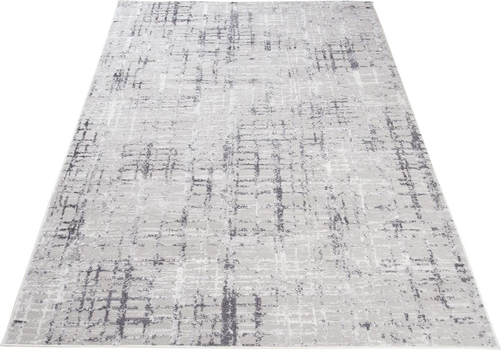 A light gray rug with a distressed geometric pattern is shown from a diagonal angle on a white background.
