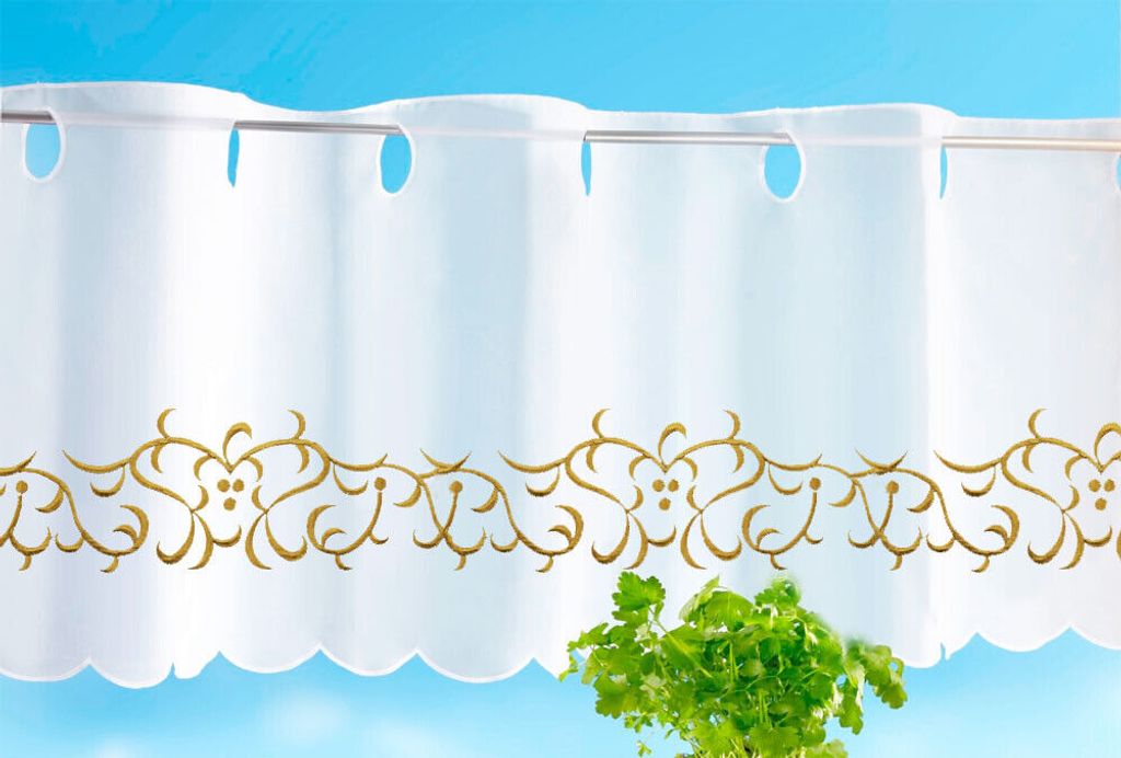 A white kitchen curtain with gold embroidery hangs against a light blue background, with a plant in the foreground.
