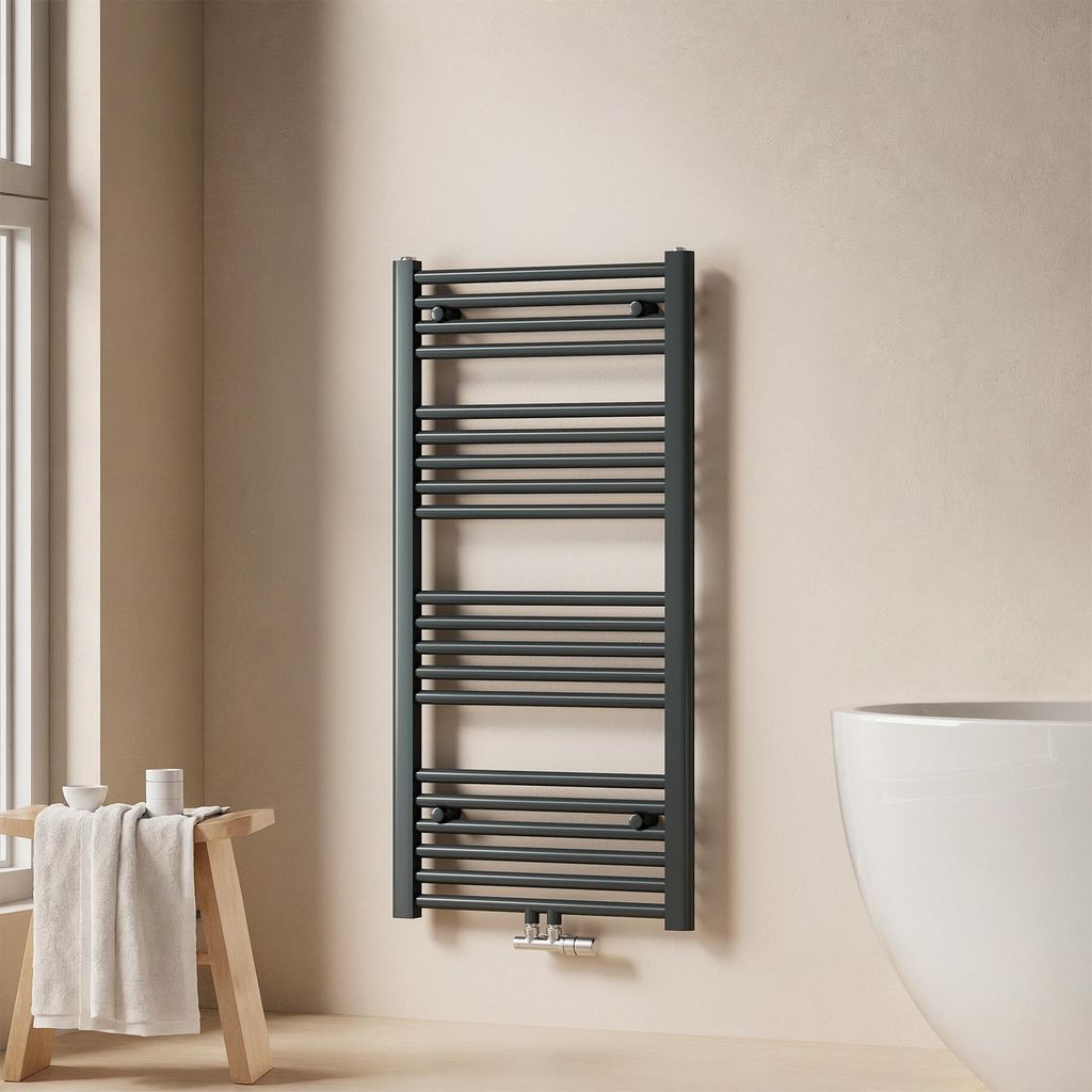 A modern bathroom setting with a dark grey towel radiator mounted on a beige wall, next to a white bathtub and a wooden stool with a folded towel.