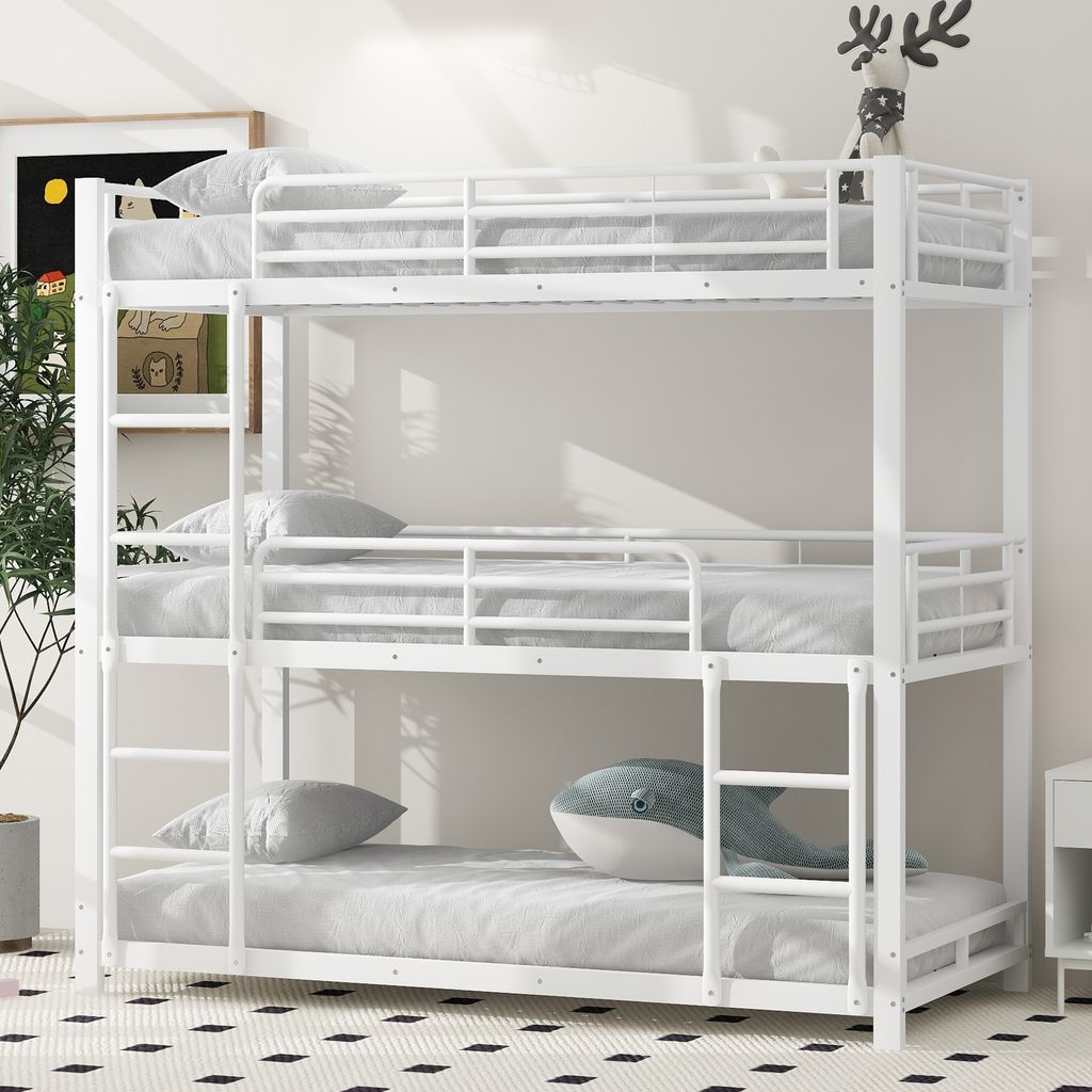 A white triple bunk bed with mattresses and pillows in a room with a patterned rug and a plant.