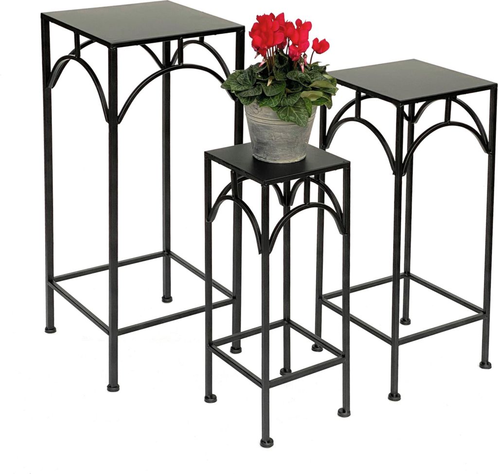 Three black metal plant stands of varying heights are arranged on a white background. A potted plant with red flowers sits on the middle stand.