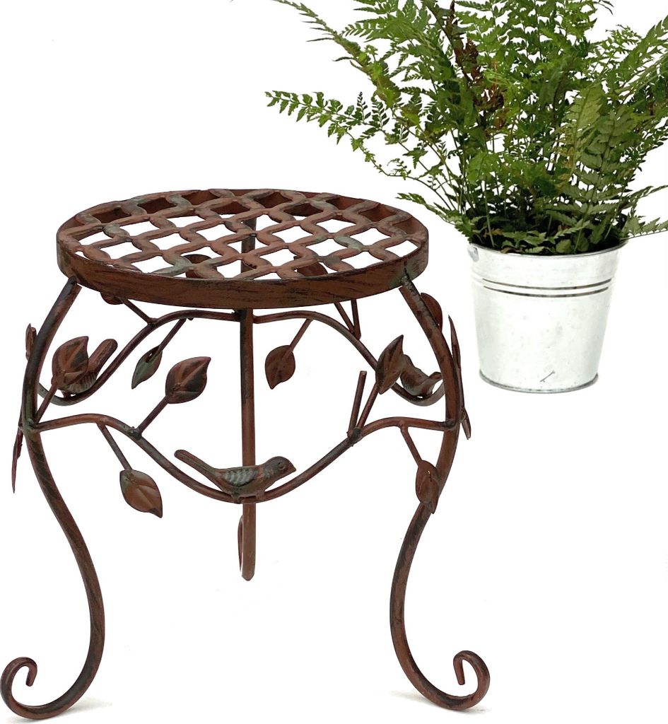 A metal plant stand with a decorative bird and leaf design, next to a potted fern in a metal bucket.