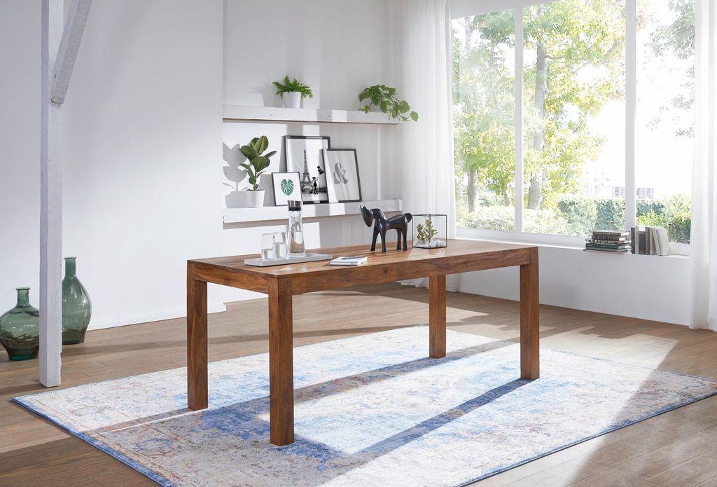 A dining room scene with a wooden table and chairs, set against a large window with natural light.