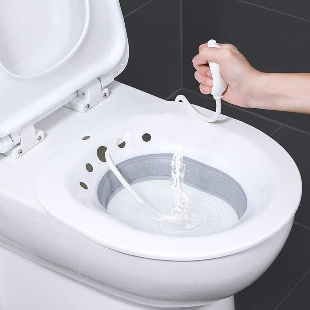A hand is holding a bidet attachment for a toilet, with water spraying into the toilet bowl.