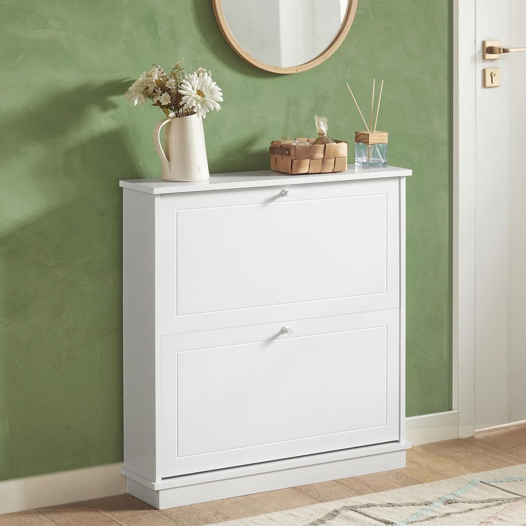 A white shoe cabinet with two drawers is shown against a green wall.