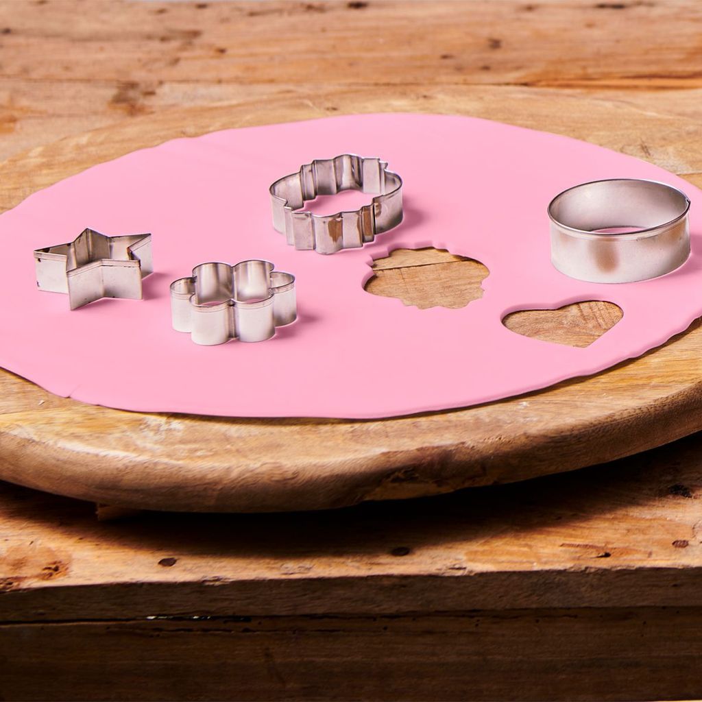 Cookie cutters are being used to cut shapes out of pink fondant on a wooden board.