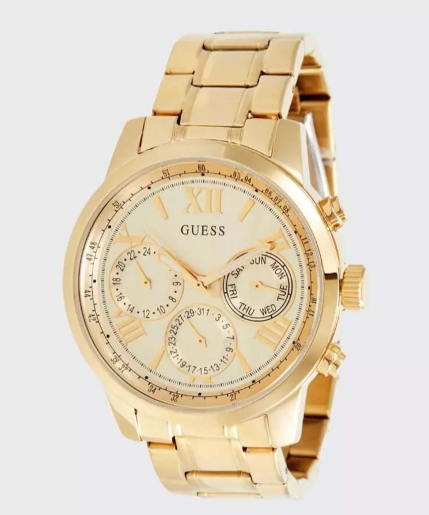 A close-up studio shot of a gold-colored Guess watch against a light gray background.