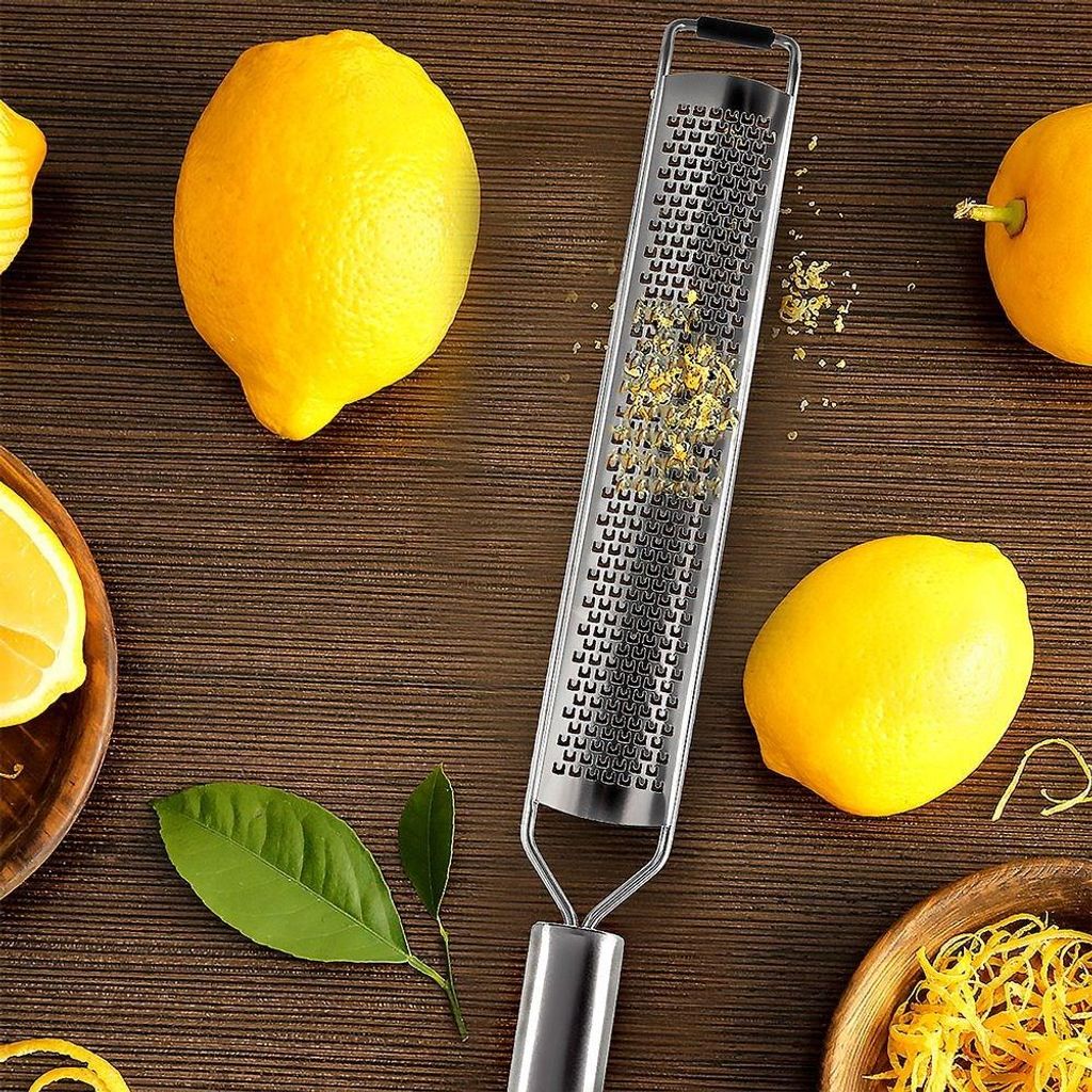 A grater with lemon zest on it, surrounded by lemons and lemon leaves on a wooden surface.