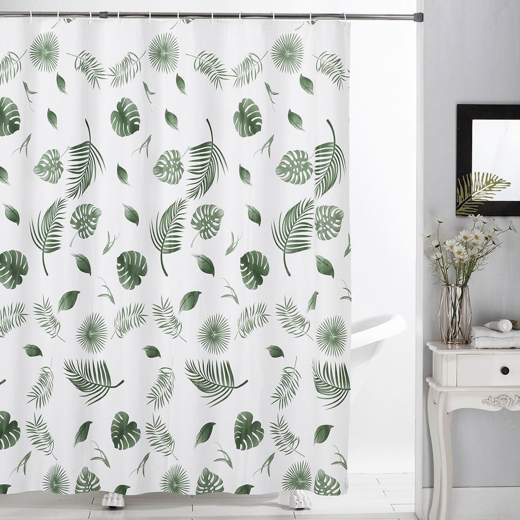 A white shower curtain with a green leaf pattern is hanging in a bathroom.