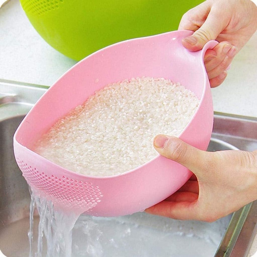 Hands holding a pink rice washing bowl filled with rice over a sink, with water draining.
