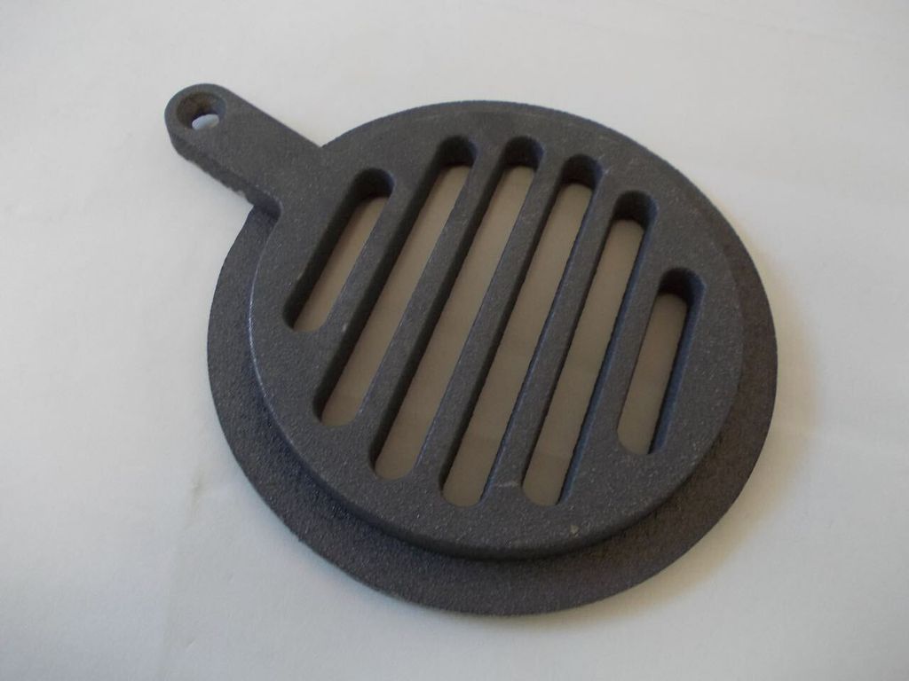 A dark gray cast iron grate with a handle and a circular base is placed on a light gray surface.