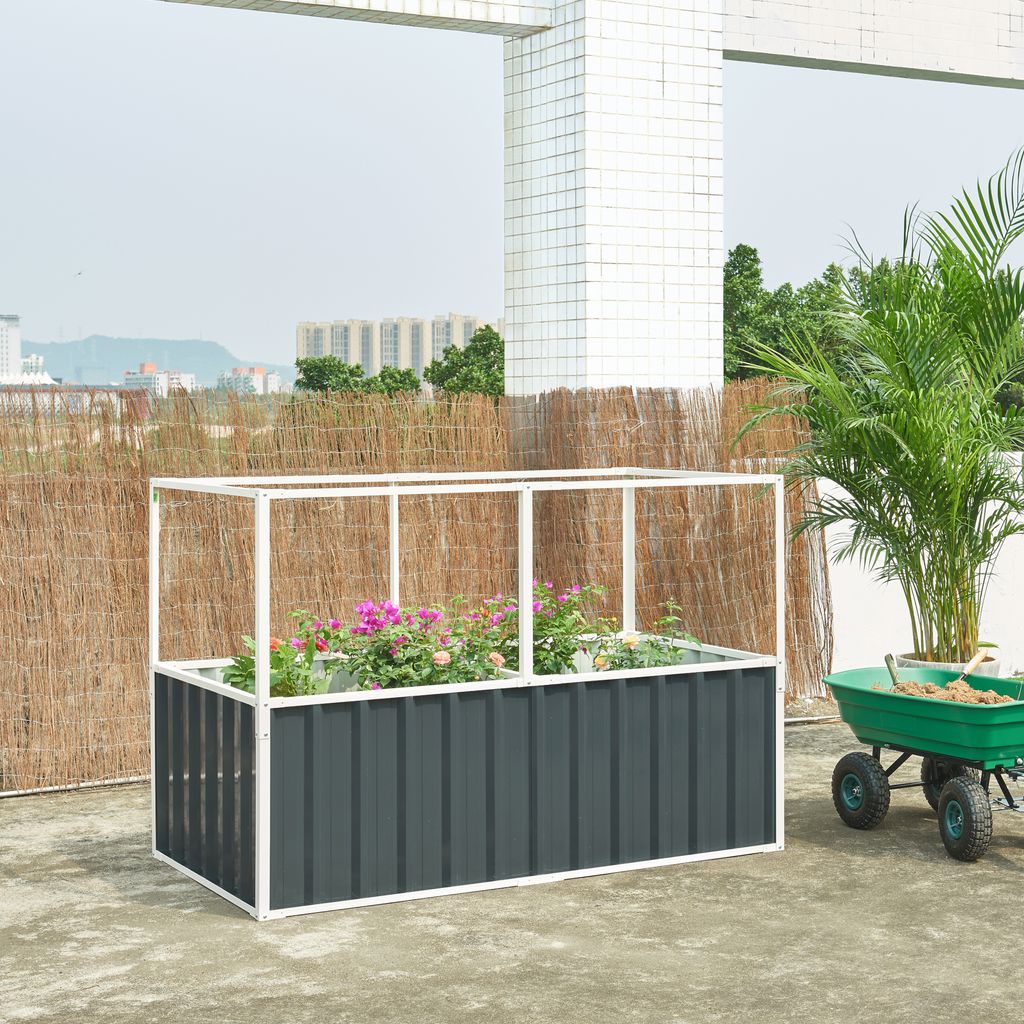 A raised garden bed with flowers on a rooftop, next to a green wheelbarrow filled with soil.