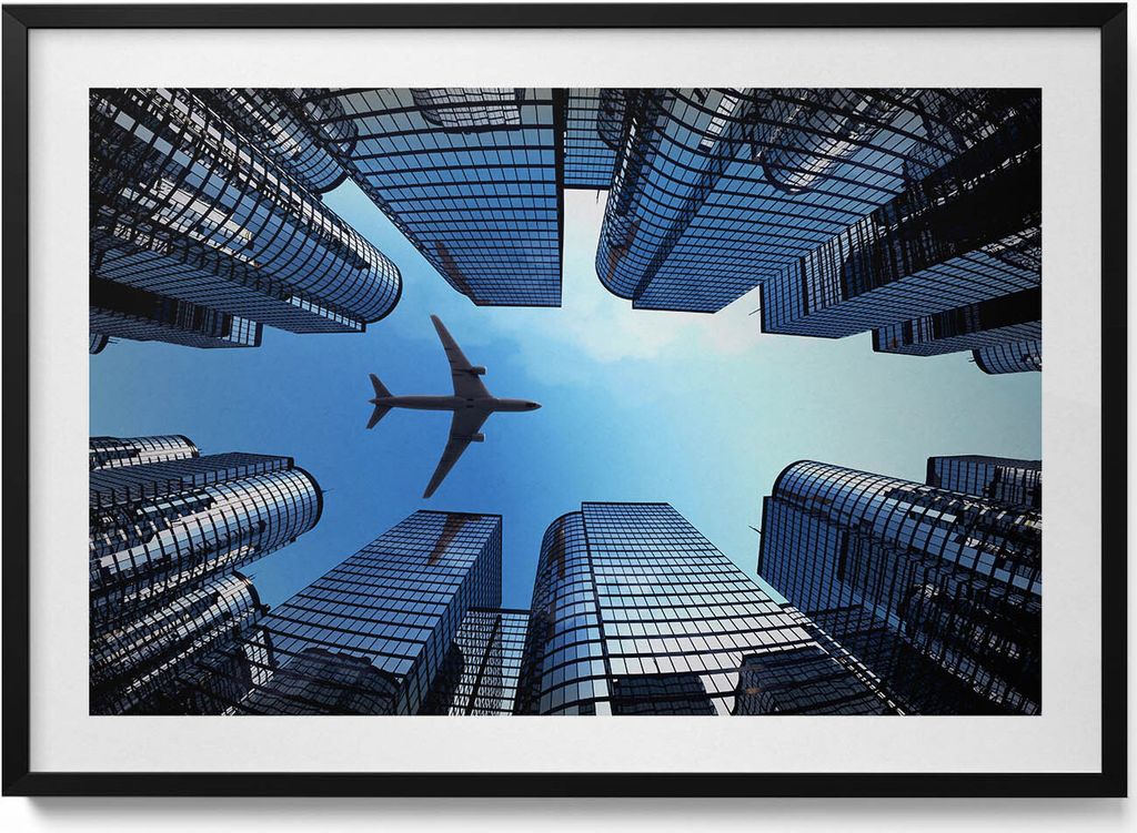Flugzeug über Gebäuden– Wandbild mit Rahmen – Gerahmtes Bild – Wanddekoration – 100x70 cm – Schwarz Rahmen