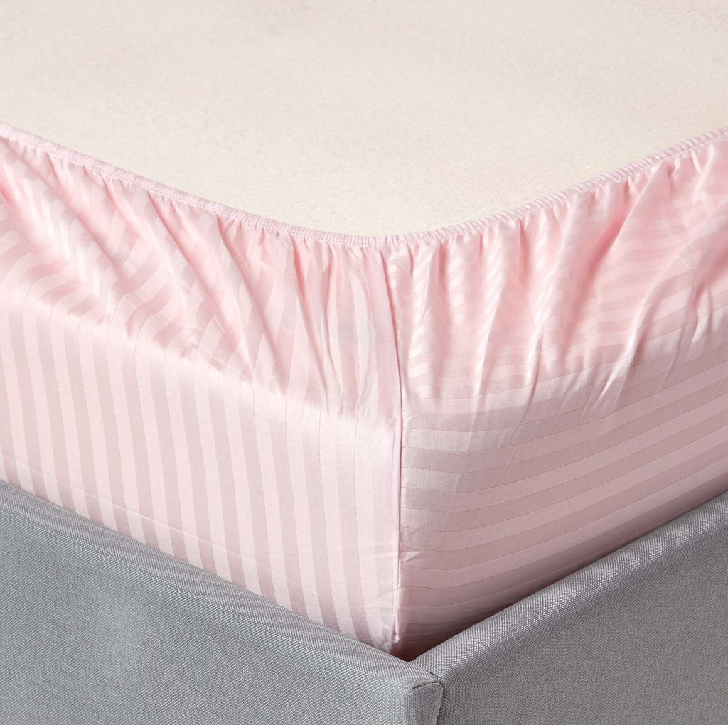 A close-up view of a pink striped fitted sheet on a bed.