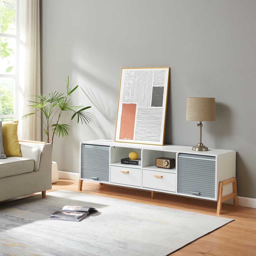 A modern living room scene featuring a white and gray media console with wooden legs, decorated with a framed abstract art piece and a table lamp.