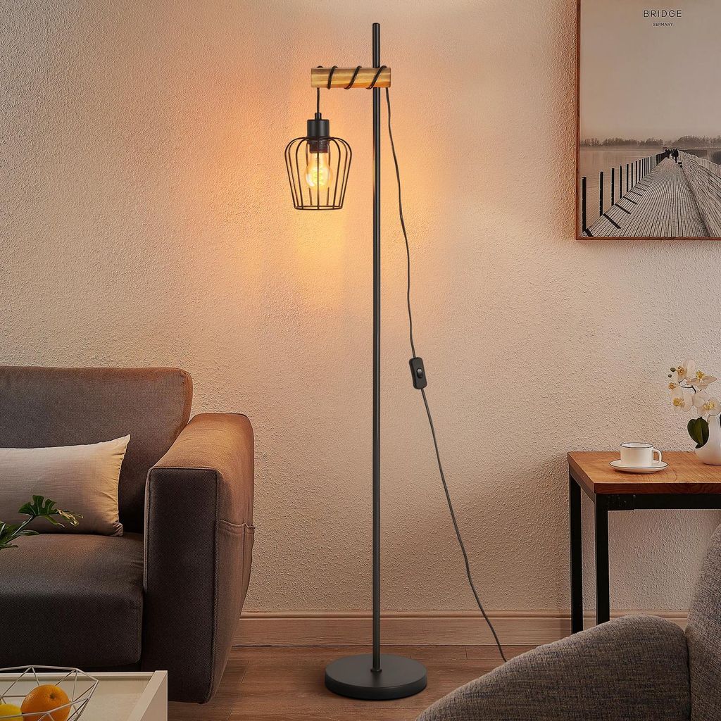 A floor lamp with a vintage industrial design is placed next to a sofa in a living room.