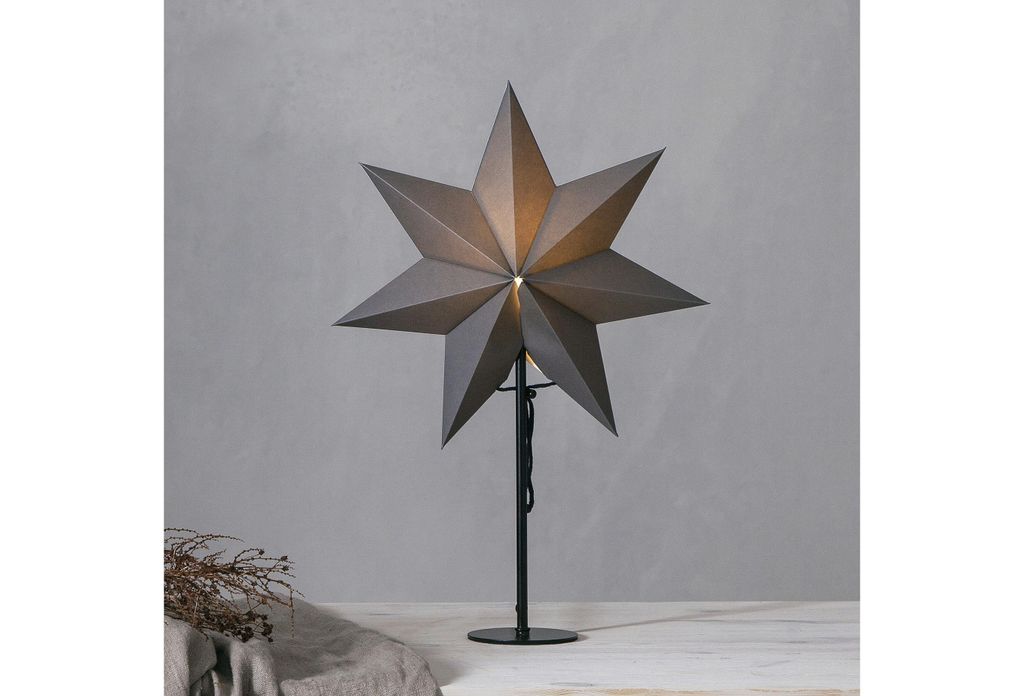 A star-shaped lamp on a stand against a gray wall.