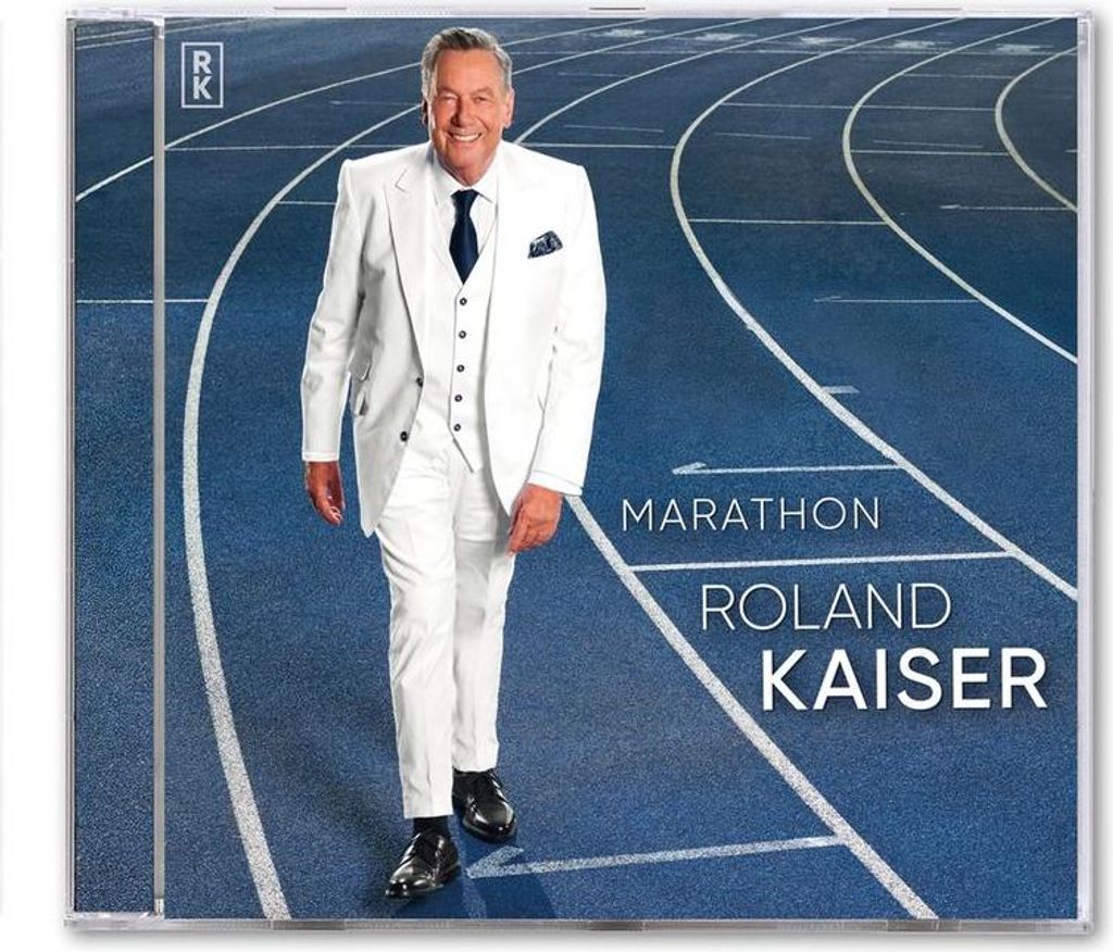 A man in a white suit walks on a blue running track.