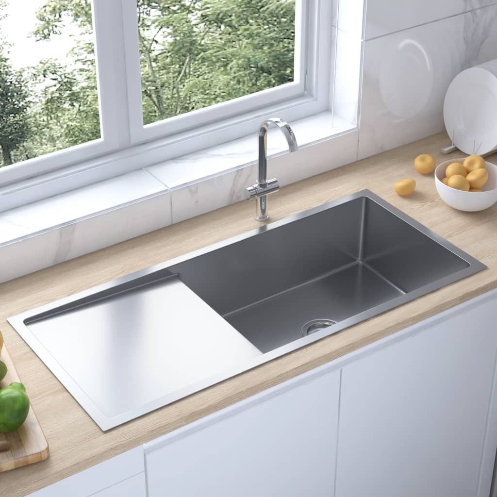 A stainless steel kitchen sink with a draining board is shown in a modern kitchen setting.