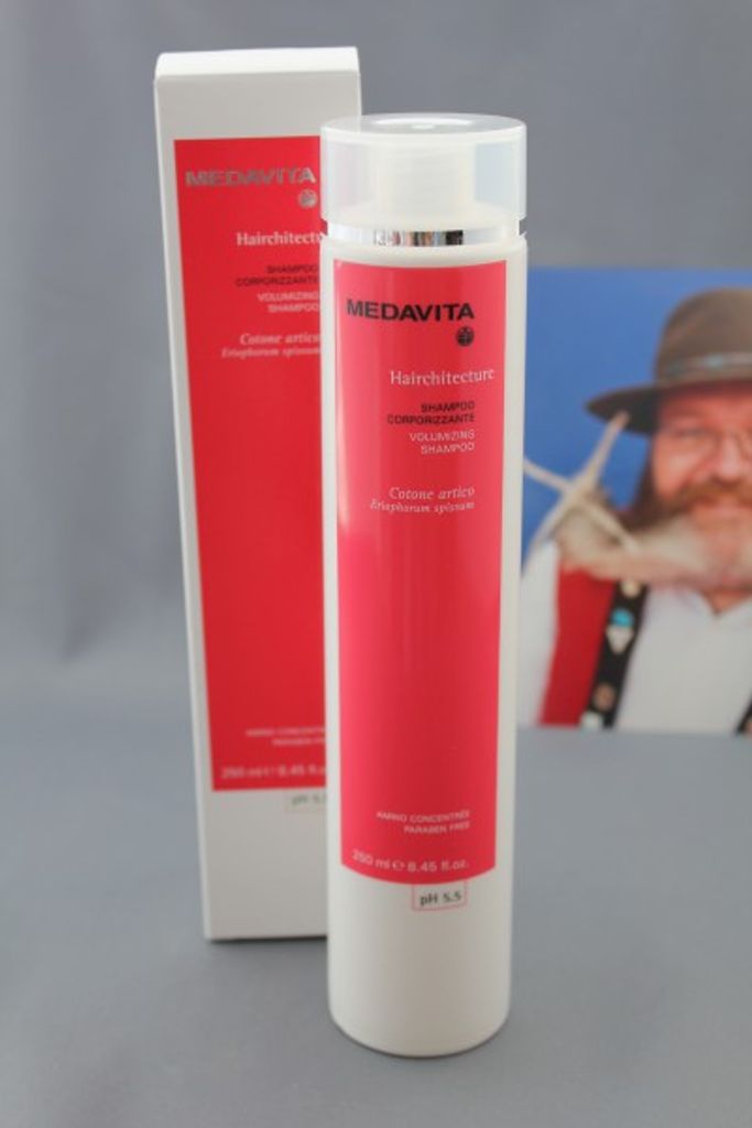 A product shot of a shampoo bottle and its packaging, with a blurred background image of a person.